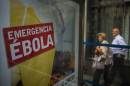 People walk by an advertising calling for financial help to fight Ebola in Africa in Madrid, Spain, Tuesday, Oct. 7, 2014. Three more people were placed under quarantine for Ebola at a Madrid hospital where a Spanish nurse became infected, authorities said Thursday. More than 50 other possible contacts were being monitored. The nurse, who had cared for a Spanish priest who died of Ebola, was the first case of Ebola being transmitted outside of West Africa, where a months-long outbreak has killed at least 3,500 people and infected at least twice as many. (AP Photo/Andres Kudacki)