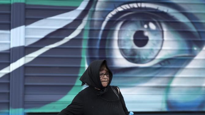 A woman walks past graffiti by street artist Achilles outside a shop, in Athens, Greece, on Thursday June 4, 2015. Greece remains at loggerheads with creditors over key economic reforms after a meeting between Prime Minister Alexis Tsipras and the head of the European Union&#39;s executive arm failed to yield a breakthrough on the release of vital bailout loans. (AP Photo/Petros Giannakouris)