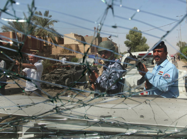 Iraqi security forces, seen through the broken glass of a police car, inspect the site where a suicide car bomber plowed his vehicle into a checkpoint outside a police building just outside the holy city of Najaf, Iraq, Monday, Aug. 15, 2011. Bomb blasts ripped through more than a dozen Iraqi cities Monday morning, killing scores of people _ most of them in the southern city of Kut _ in a wave of violence that shattered what had been a relatively peaceful holy month of Ramadan. The violence struck from the northern city of Kirkuk to the capital of Baghdad to the southern Shiite cities of Najaf, Kut and Karbala, and emphasized the persistent ability of insurgents to wreak havoc at a time when Iraqi officials are weighing whether they are able to protect the country without the assistance of American troops. (AP Photo/Alaa al-Marjani)