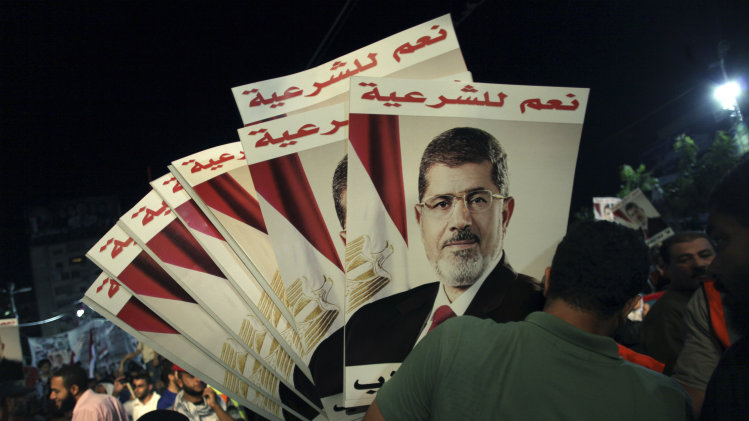 A supporter of Egypt's ousted President Mohammed Morsi holds his posters with Arabic writing which reads " Yes for legality," during a protest outside Rabaah al-Adawiya mosque, where protesters have installed a camp and hold daily rallies at Nasr City in Cairo, Egypt, Tuesday, Aug. 6, 2013. (AP Photo/Khalil Hamra)