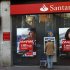 A man uses an ATM machine as another talks on the phone outside a Santander bank branch in Madrid