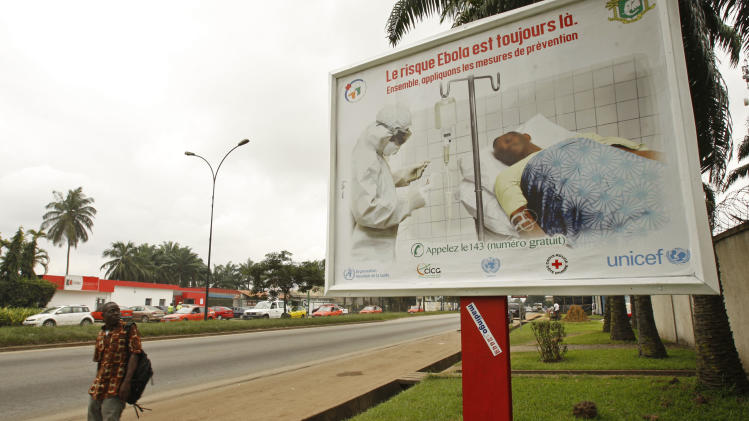A man, left, walk past a Ebola awareness campaign poster, in the city of Abidjan, Ivory Coast, Monday, Aug. 25, 2014. (AP Photo/Sevi Herve Gbekide )