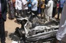 People gather around a car used by a suicide bomber at a catholic church in Jos, Nigeria, on Sunday, March 11, 2012. A suspected suicide attack hit a Catholic church in the central Nigerian city of Jos on Sunday, killing three people, the National Emergency Management Agency (NEMA) said. (AP Photos)
