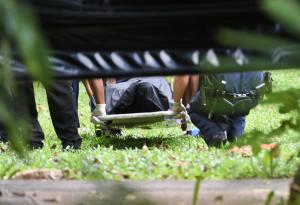 Police carry away a gun shot victim in a body bag behind …