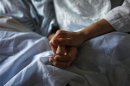 A woman holds the hand of her mother who is dying from cancer during her final hours at a palliative care hospital in Winnipeg