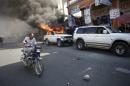 A man riding a bike passes next to a car that was set afire by protesters during a demonstration against the electoral process in Port-au-Prince, Haiti