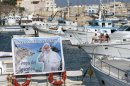 A poster reading "Welcome Pope Francis, the fishermen's Pope" is displayed on a boat moored at the Lampedusa harbor, Italy, Sunday, July 7, 2013. Pope Francis heads Monday to the Sicilian island of Lampedusa for his first pastoral visit outside Rome, going to the farthest reaches of Italy to pray with migrants who have recently arrived and remember those who have died trying. Francis, a pope from "the end of the Earth" whose ancestors immigrated to Argentina from Italy, has a special place in his heart for refugees: As archbishop of Buenos Aires, he denounced the exploitation of migrants as "slavery" and said those who did nothing to stop it were complicit by their silence. On Monday, he will arrive at Lampedusa's port by boat and will throw a floral wreath into the sea in memory of those who died trying to reach the island, which is closer to Africa than the Italian mainland. (AP Photo/Gregorio Borgia)
