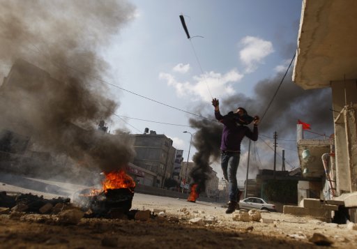 A Palestinian protester uses a sling to hurl stones at Israeli security officers during clashes at a demonstration marking Land Day near Ramallah