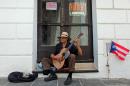 A man plays his guitar while he begs for money in front of a closed down business in Old San Juan, Puerto Rico, Monday, June 29, 2015. International economists released a critical report on Puerto Rico's economy Monday on the heels of the governor's warning that the island can't pay its $72 billion public debt. (AP Photo/Ricardo Arduengo)