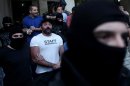 Lawmakers of the extreme far-right Golden Dawn party Yannis Lagos (front) and Ilias Kasidiaris (back) are escorted by masked police officers to the prosecutor from the police headquarters in Athens on September 28, 2013