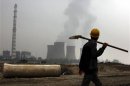 A coal-burning power station can be seen behind a migrant worker on the outskirts of Beijing