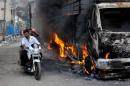 Men ride a motorcycle past a lorry which was set on fire by protesters in Bengaluru