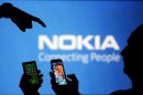 Men are silhouetted against a video screen with an Nokia logo as he poses with an Nokia Lumia 820 and Samsung S4 smartphones in this photo illustration taken in the central Bosnian town of Zenica