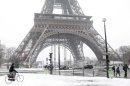 A man rides bicycle as he makes his way along a snow-covered sidewalk near the Eiffel Tower in Paris