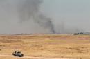 A vehicle drives as smoke billows from an area controlled by jihadist militants from the Islamic State of Iraq and the Levant (ISIL) following clashes with Shiite Turkmen on June 29, 2014 in the Iraqi village of Bashir