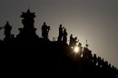 The sun sets behind the statues on top of the Bernini colonnade in St. Peter Square, at the Vatican, Monday, March 4, 2013. Cardinals from around the world have gathered inside the Vatican for their first round of meetings before the conclave to elect the next pope, amid scandals inside and out of the Vatican and the continued reverberations of Benedict XVI's decision to retire. (AP Photo/Andrew Medichini)