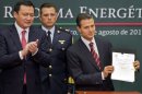 Mexico's President Enrique Pena Nieto, right, shows to the audience his proposal that would allow private firms to participate in the oil industry as his Interior Secretary Miguel Angel Osorio Chong applauds in Mexico City, Monday, Aug.12, 2013. Pena Nieto is making his most daring gamble yet, with a proposal to lift a decades-old ban on private companies in the state-run oil industry, a cornerstone of Mexico's national pride. (AP Photo/Eduardo Verdugo)