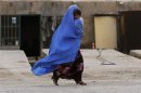 Una donna afghana coperta dal burqa corre tenendo suo figlio in braccio per le strade di Kabul