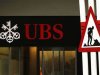 A woman woman walks past a construction road sign in front of a branch of Swiss Bank UBS in Lugano