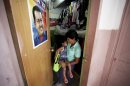 In this Sept. 27, 2012 photo, a poster of Venezuela's President Hugo Chavez hangs on the door where Maria Perez carries her granddaughter out of the room where they live that was once a school room and is now part of a government provided shelter for families who lost their homes due to flooding, in Caracas, Venezuela. Fear of every stripe, like the loss of government housing like this one, permeates the intensely polarized election campaign, with many votes to be decided based not on the candidates' promises but rather on what worries people most. Chavez has continuously warning of chaos and the dismantling of the generous welfare state he built if he is voted out of office in the Oct. 7 vote. (AP Photo/Fernando Llano)