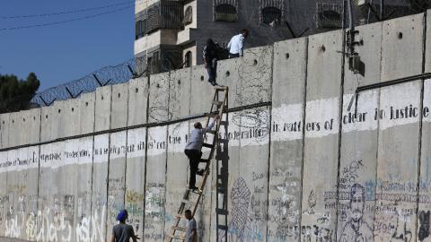 Palestinians climb over a section of Israel's separation barrier, near Qalandia checkpoint between Ramallah and Jerusalem, in July 2015