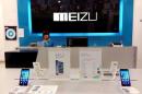 Shop assistant waits for customers at a Meizu store as Meizu MX3 smartphones are seen on display in the foreground, in Shenzhen