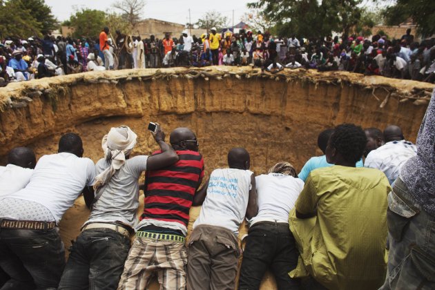 People watch a traditional ceremony taking place in a large former well in the village of Ndande