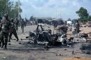 Military officers walk past the remains of a car after an explosion on July 23, 2014 in Kaduna, Nigeria