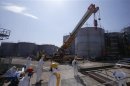 Tecnici con tute e maschere protettive al lavoro vicino a tank di acque contanimante nell'impianto nucleare giapponese di Fukushima Daiichi, gestito da Tepco