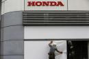 Workers stand under the logo of Honda Motor Co. outside the company's headquarters in Tokyo