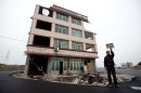 Luo Baogen holds his land certificate as he stands next to his house in the middle of a newly built road in Wenling city in east China's Zhejiang province Thursday, Nov. 22, 2012. Luo, the owner of the house, refused to sign an agreement to allow his house to be demolished by the authorities, as the compensation offered to him was not enough, according to local media. (AP Photo)