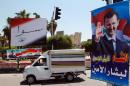 FILE - In this May 12, 2014 file photo, a vehicle drives past campaign posters of the June 3 presidential election in Damascus, Syria. Workers tore down towering campaign posters Monday and soldiers searched cars entering Damascus on the eve of Syria's presidential elections, which incumbent Bashar Assad is widely expected to win despite the nation's devastating civil war that began as a peaceful revolt against his rule. The Arabic on the poster, right, reads, "Damascus spreads flowers for the loyal Bashar." The banner, left, reads, "Together with Bashar Assad." (AP Photo, File)