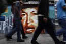 People walk by a mural of Venezuela's President Hugo Chavez in Caracas, Venezuela, Friday, April 20, 2012. Chavez is in Cuba to continue with cancer treatment. (AP Photo/Ariana Cubillos)