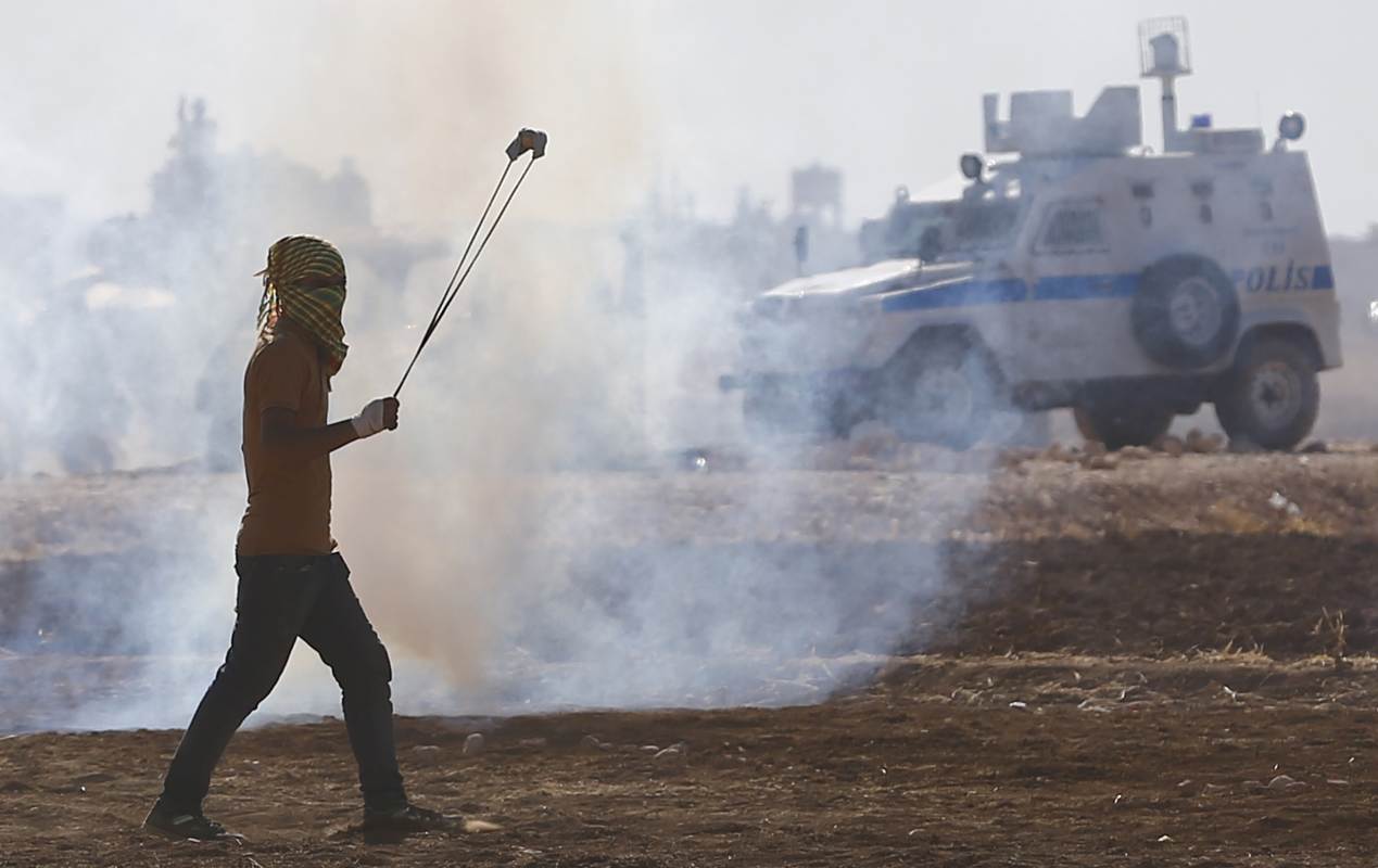 A Turkish Kurd protester swings a slingshot during clashes with Turkish security forces near Suruc