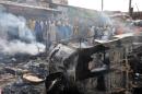 People gather to look at a burnt vehicle following a bomb explosion that rocked the roundabout near the crowded Monday Market in Maiduguri, Borno State, on July 1, 2014