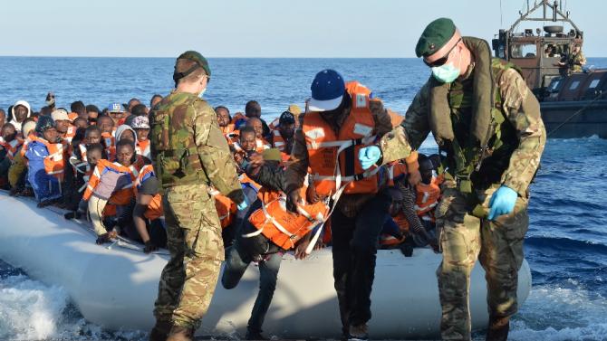 British Royal Marines help migrants disembark from an inflatable boat onto a landing craft of HMS Bulwark after being rescued around 40 miles off the coast of Libya on May 13, 2015