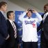 Dodgers' new left-handed pitcher Hyun-Jin Ryu of South Korea wears a cap as he puts on his new jersey while standing with general manager Colletti, owner Magic Johnson, and his agent Boras at a news conference in Los Angeles