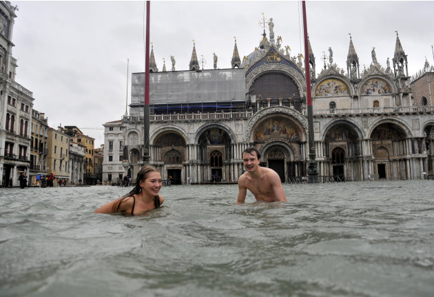 A young man and a woman enjoy swimming in flooded St. Mark's Square in Venice, Italy, Sunday, Nov. 11, 2012. High tides have flooded Venice, leading Venetians and tourists to don high boots and use wo