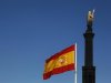 A Spanish flag flutters in the wind near a statue of Columbus in Madrid