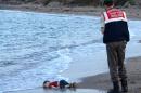 A Turkish police officer stands next to the body of a migrant child on the shores in Bodrum, southern Turkey, on September 2, 2015 after a boat carrying refugees sank while trying to reach the Greek island of Kos