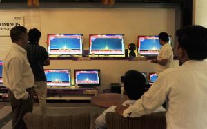 Indian bystanders watch a bank of screens showing the …