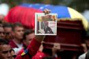 A person holds up a photograph of former Venezuelan Intelligence Chief Eliezer Otaiza as his flag-draped coffin is carried outside the National Assembly during a funeral procession in Caracas, Venezuela, Wednesday, April 30, 2014. Otaiza's body was dumped on the edge of Caracas Saturday after his vehicle was intercepted by a group of armed men. No motive has been established for the crime. As a young army officer, he backed Hugo Chavez's failed 1992 coup attempt and was responsible for his personal security when he was elected president in 1998. (AP Photo/Fernando Llano)