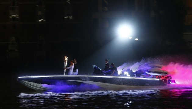 Britain's David Beckham drives a powerboat with the Olympic torch as fireworks are launched over Tower Bridge during the opening ceremony of the London 2012 Olympic Games