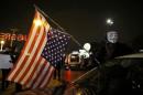 A protester wearing a Guy Fawkes mask holds the U.S. flag outside the Ferguson Police Department in Ferguson