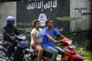 In this March 8, 2014 photo, motorists ride past a graffiti of the Islamic State group's flag in Solo, Central Java, Indonesia. The world's largest Muslim country is facing a new threat as security officials fear that militants who are joining the Islamic State could take part in terrorism acts on their return to Southeast Asia. (AP Photo)