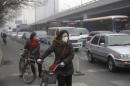 File photo of a woman wearing a mask stands besides her bicycle as vehicles stop at a traffic junction on a busy street amid thick haze in Beijing