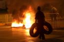 A Sunni protestor carries tires as a fire set by Sunni protesters burns on a major roadway between Beirut and the capital's southern suburbs, a Hezbollah stronghold, to show support for residents of the Sunni town of Arsal, in Beirut, Lebanon, Tuesday, March 18, 2014. Gunmen from Lebanon's militant Hezbollah group and local Shiite Muslim residents tightened their blockade of a Sunni town of Arsal near the Syrian border Tuesday, sparking concerns that thousands of Syrian refugees stranded in the area could be cut off from humanitarian aid. (AP Photo/Hussein Malla)