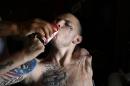 With a tattoo that reads in Chinese "warrior" on his face, Jerral Hancock, a 27-year-old Iraq war veteran who lost his left arm and is paralyzed from the waist down in a bomb explosion in Iraq, drinks soda with the help of his stepfather Dirrick Benjamin at his mobile home on Monday, Oct. 21, 2013, in Lancaster, Calif. The seniors in Jamie Goodreau's high school history class learned Hancock was stuck in a modest mobile home for months, unable to travel the 70 miles to the nearest VA hospital in Los Angeles to have his bedsores treated or his rotting teeth fixed. Goodreau's students, who each year raise a few thousand dollars for veterans, decided to make Hancock their cause. (AP Photo/Jae C. Hong)