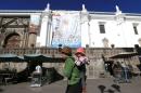 A woman holding her baby walks by a banner of Pope Francis' upcoming visit to the country at the main square in Quito