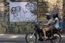 A couple riding a motorcycle, pass in front of a drawing depicting Brazil's President Dilma Rousseff, and rival candidate Marina Silva kissing each other, made by artist Cela Luz, in Rio de Janeiro, Brazil, Monday, Sept. 29, 2014. Brazil will hold general elections on Oct. 5. (AP Photo/Silvia Izquierdo)